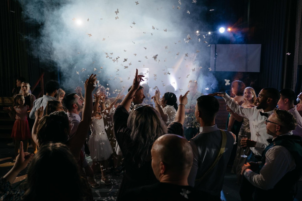 G&auml;ste feiern zum Abschluss der Hochzeit unter Konfettiregen und B&uuml;hnenlicht