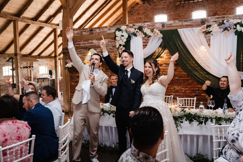 Hochzeitsmoderator und Brautpaar feiern mit den jubelnden G&auml;sten in einer rustikalen Scheunen-Location
