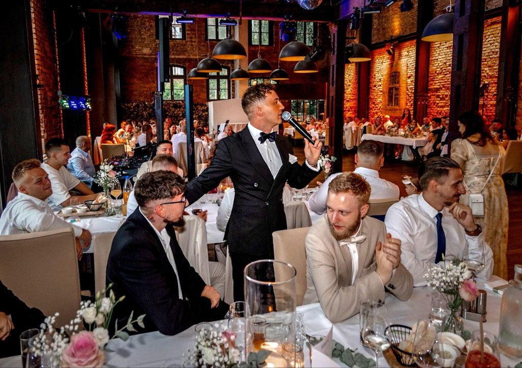 Hochzeitsmoderator in D&uuml;sseldorf f&uuml;hrt mit Mikrofon durch die Feier in einer Loft-Location